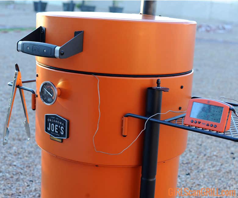 thermometer probe running under lid of orange Oklahoma Joe's Bronco Pro Drum Smoker.
