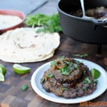 smoked and braised pork shank on black beans on white plate with tortillas and pot