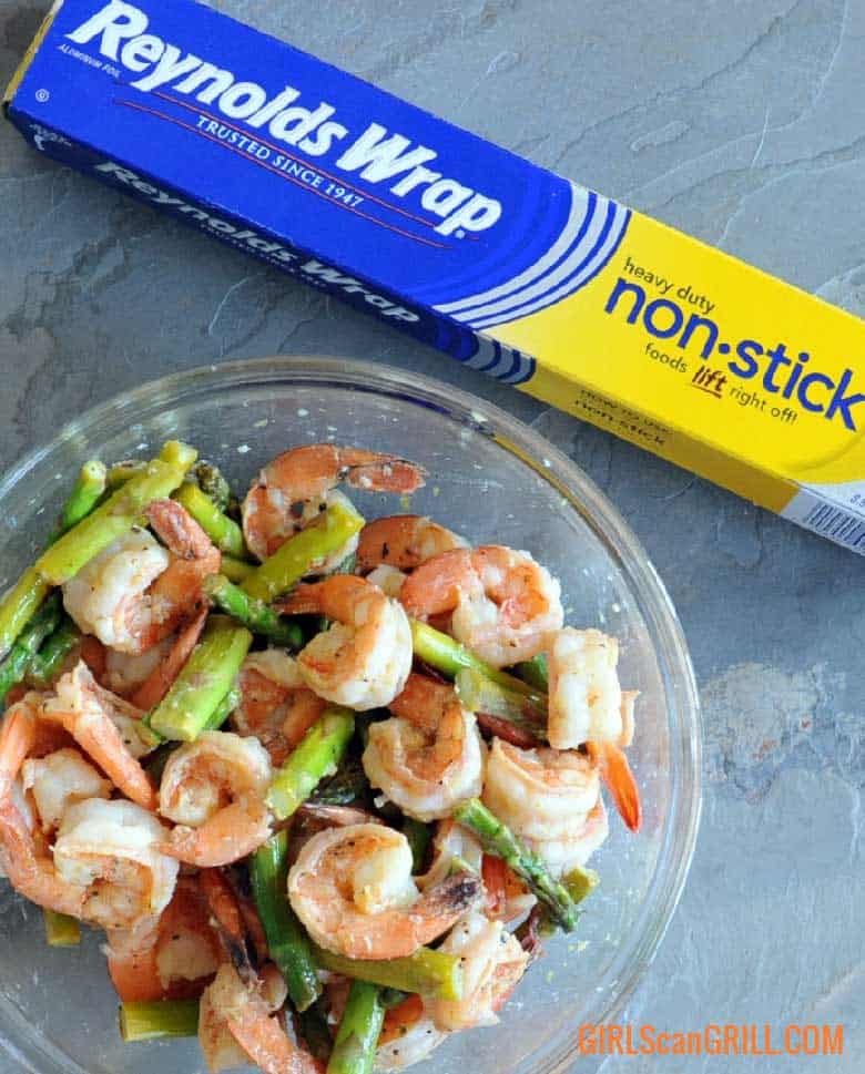 bowl of Lemon Garlic Butter Grilled Shrimp and Asparagus with box of Reynolds Wrap® Non-Stick Aluminum Foil