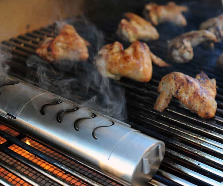 smoke flowing out of smoker set next to grilled chicken wings