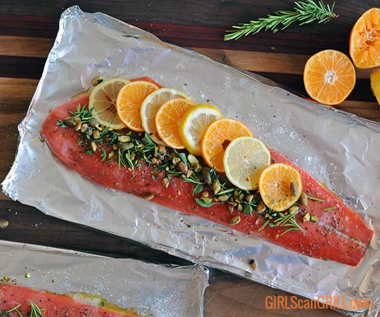 salmon fillet topped with citrus, herbs and nuts on foil.