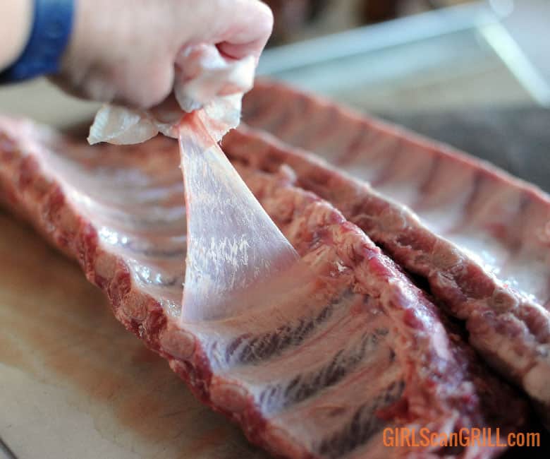 hand using paper towel to pull the membrane off of a back of ribs