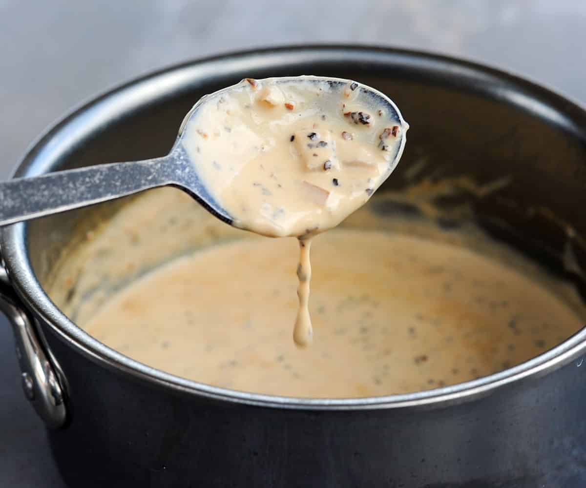 spoon with thick creamy peppercorn sauce dripping off into pot.