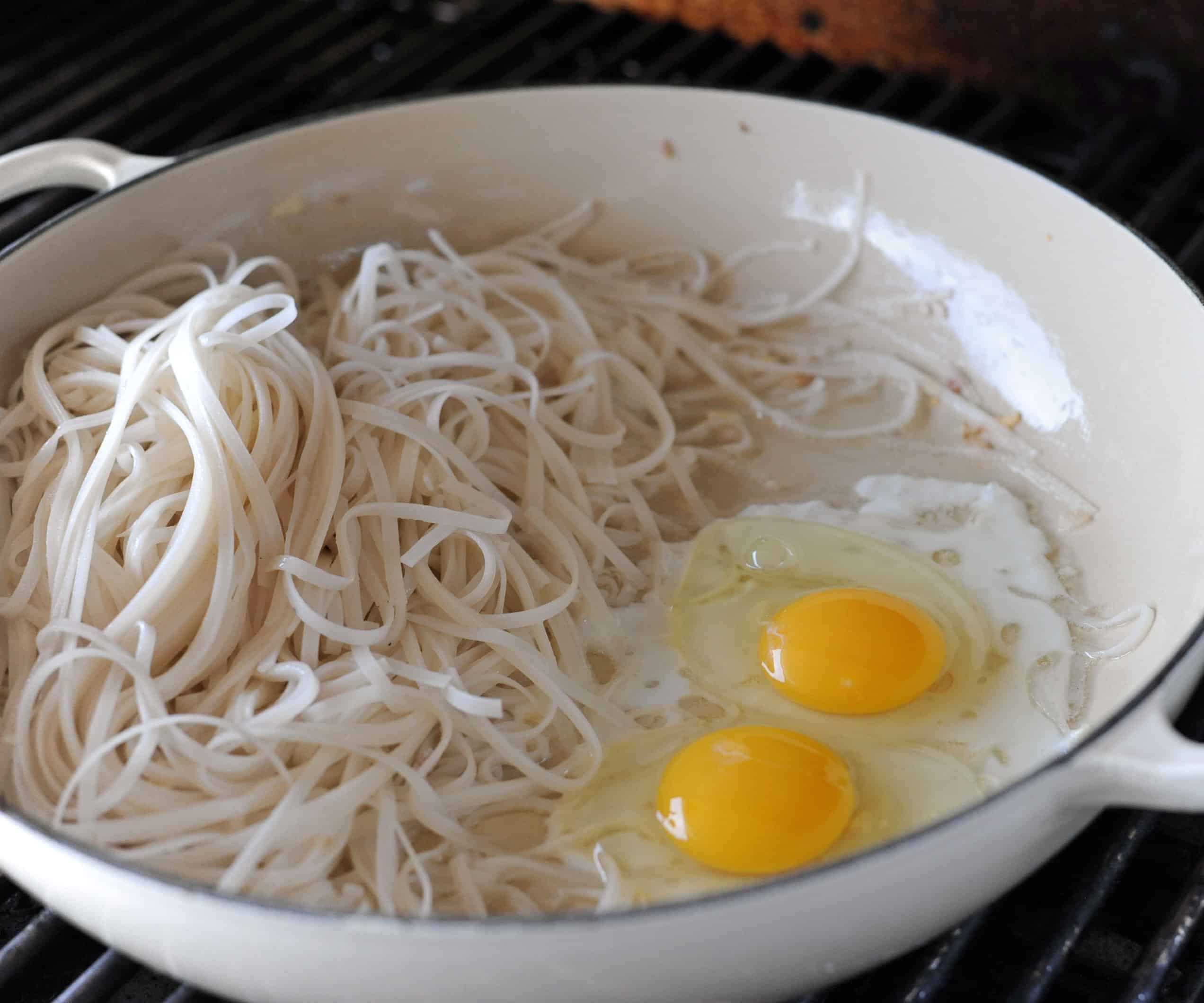 two raw eggs in a skillet next to rice noodles.