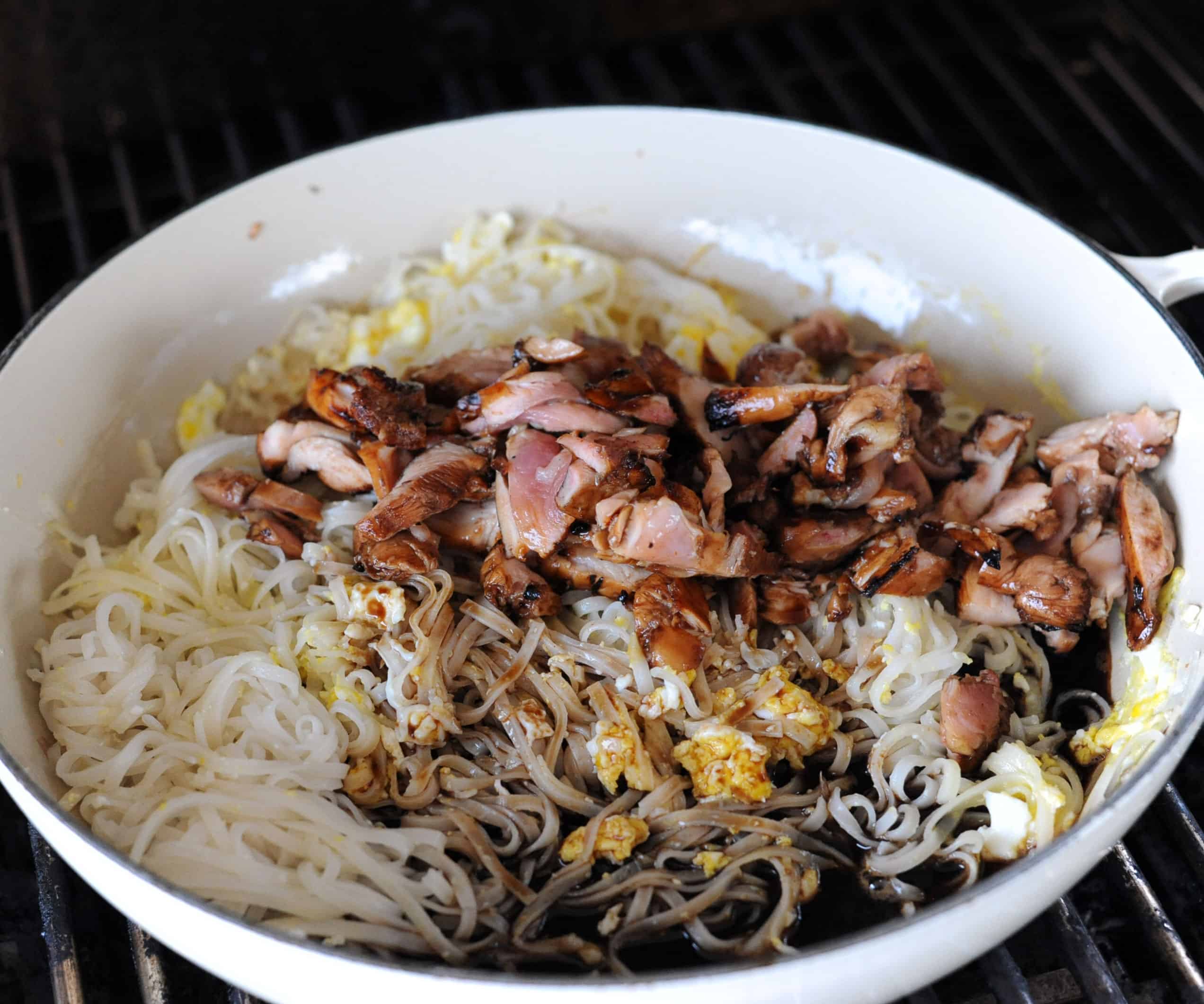 a skillet with rice noodles, cooked eggs, chicken and marinade.