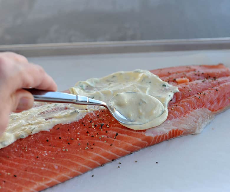 using a spoon to smear sauce on a salmon filet.