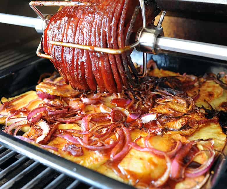 spiral ham on rotisserie over pan of pineapple and onion