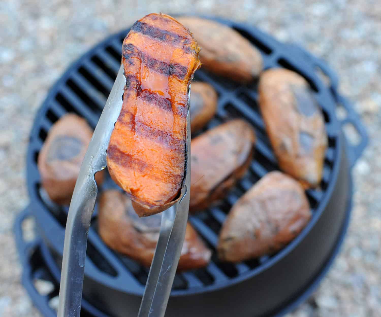 tongs holding sweet potato half with char marks.