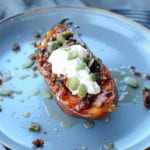sweet potato half on plate with chorizo, sour cream, pumpkin seeds