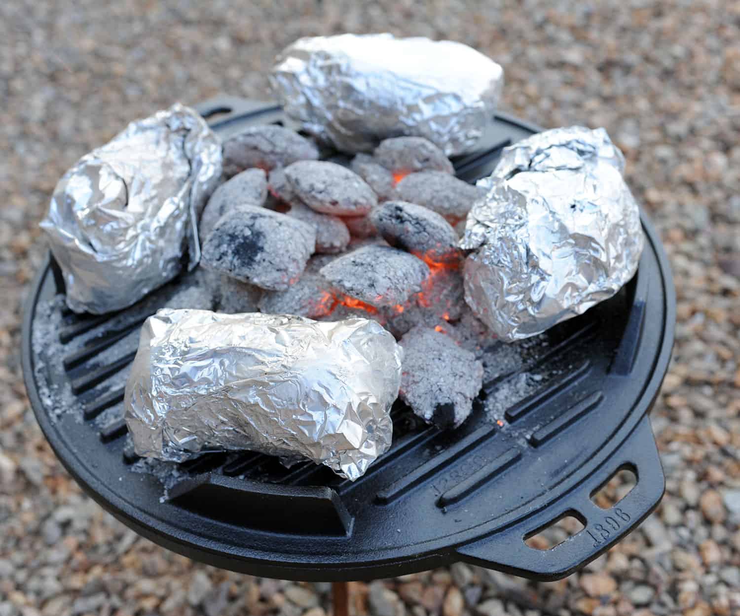 four foil-wrapped sweet potatoes on a grill.