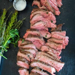 Sliced Santa Maria-style tri-tip on a platter with an herb brush.