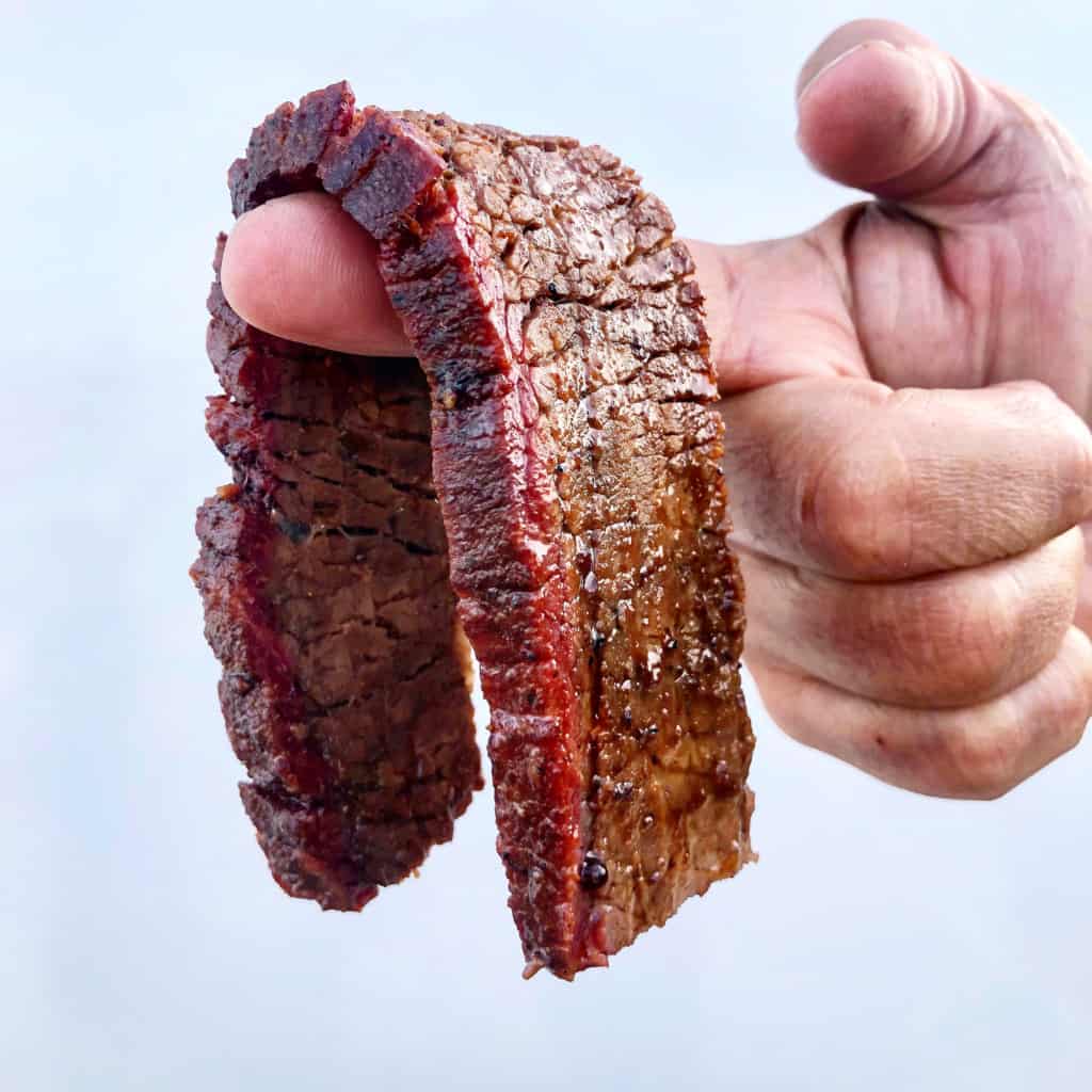 thick slice of smoked brisket draped over finger