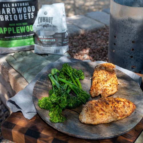 plate of two chicken breasts and broccoli by bag of Cowboy Charcoal