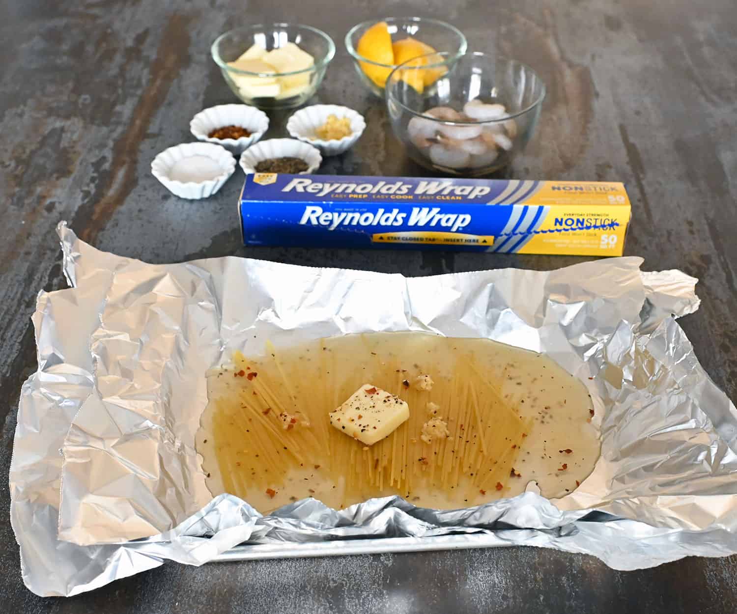 sheet of foil with noodles, butter and broth on top