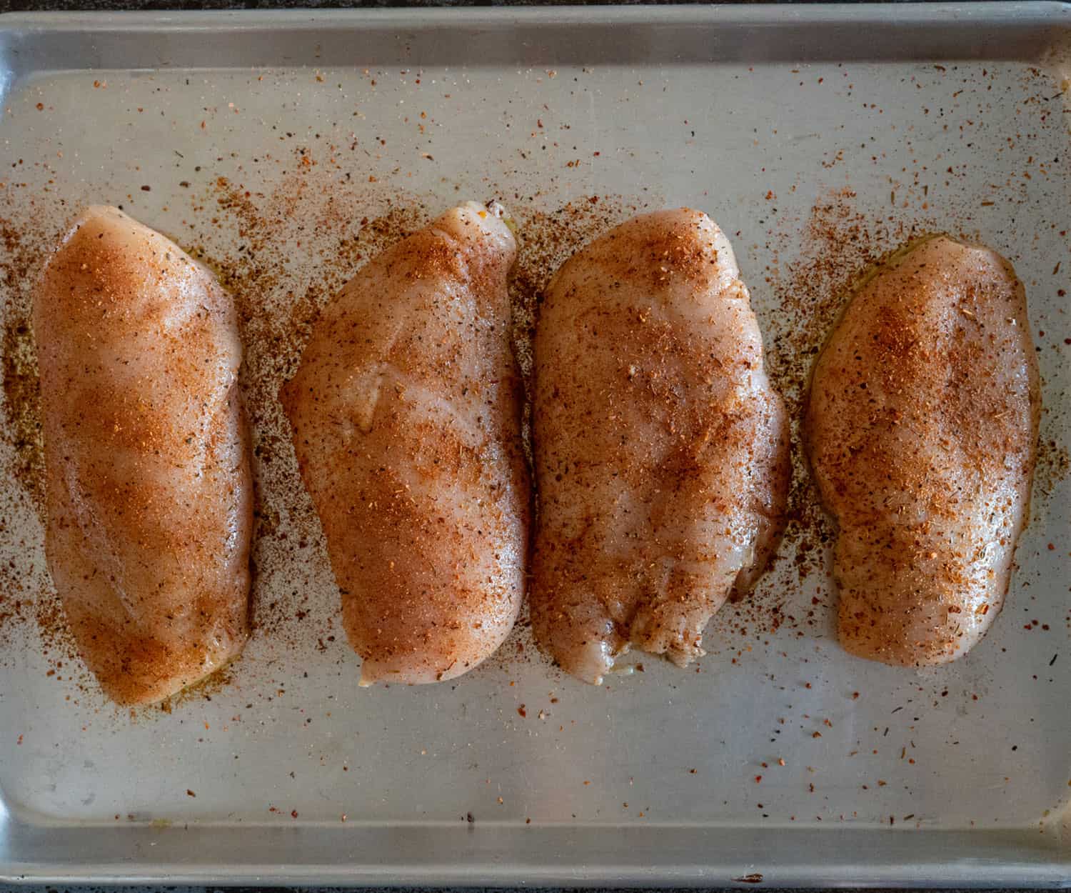 four chicken breasts on pan seasoned with rub