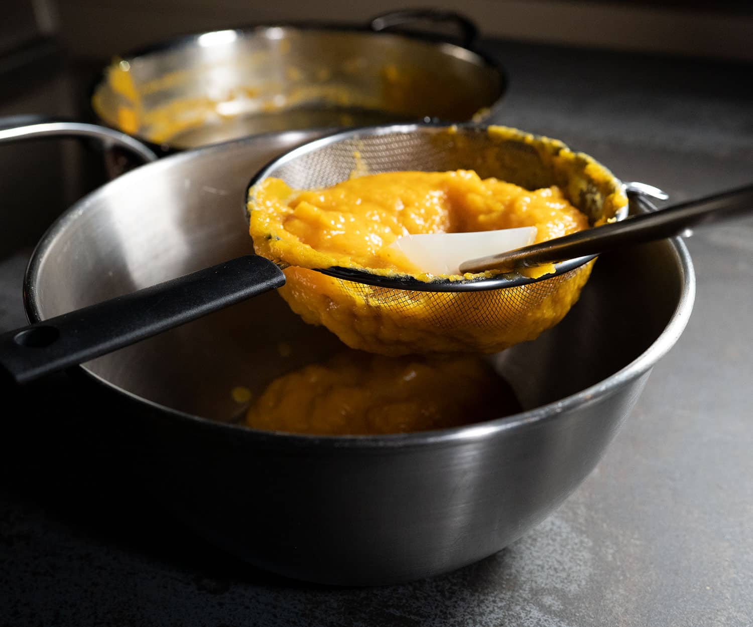 pushing grilled butternut squash through strainer