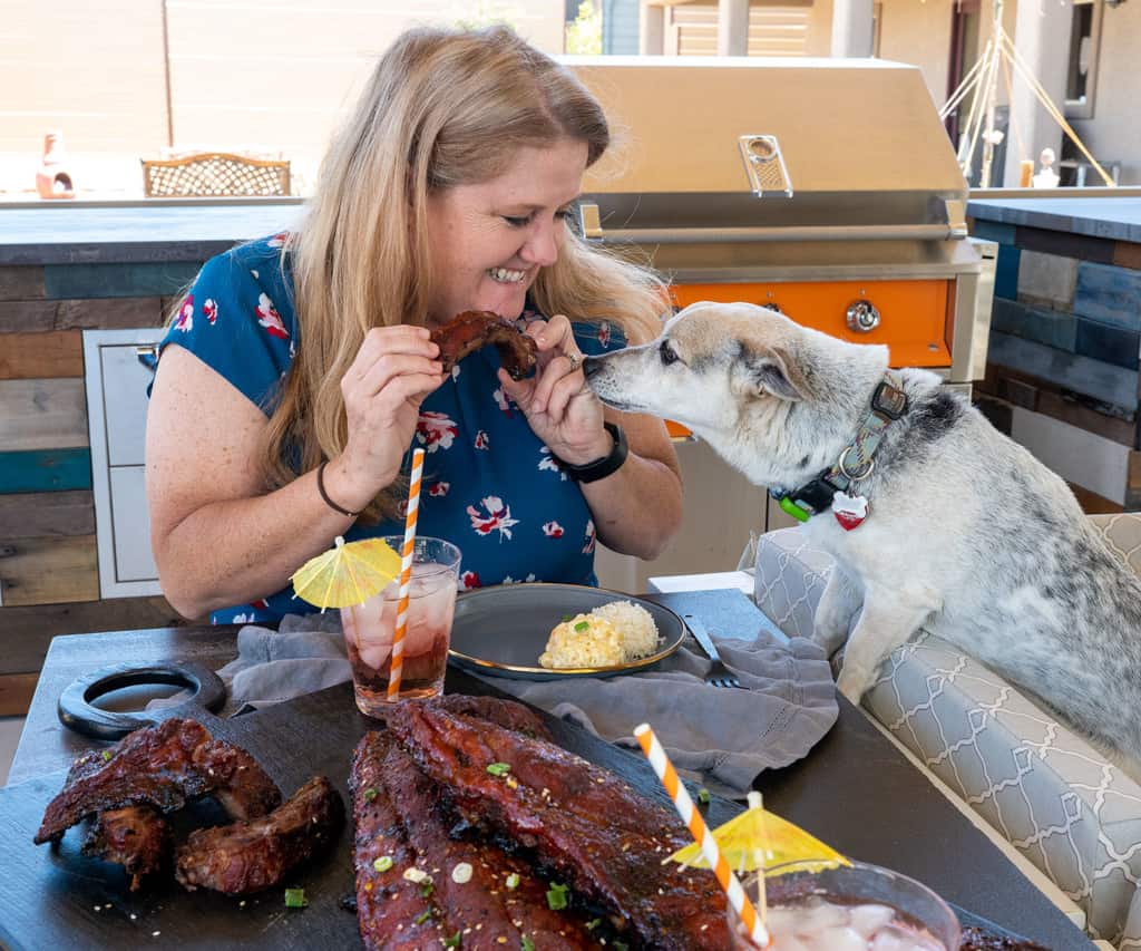 woman eating ribs with dog watching