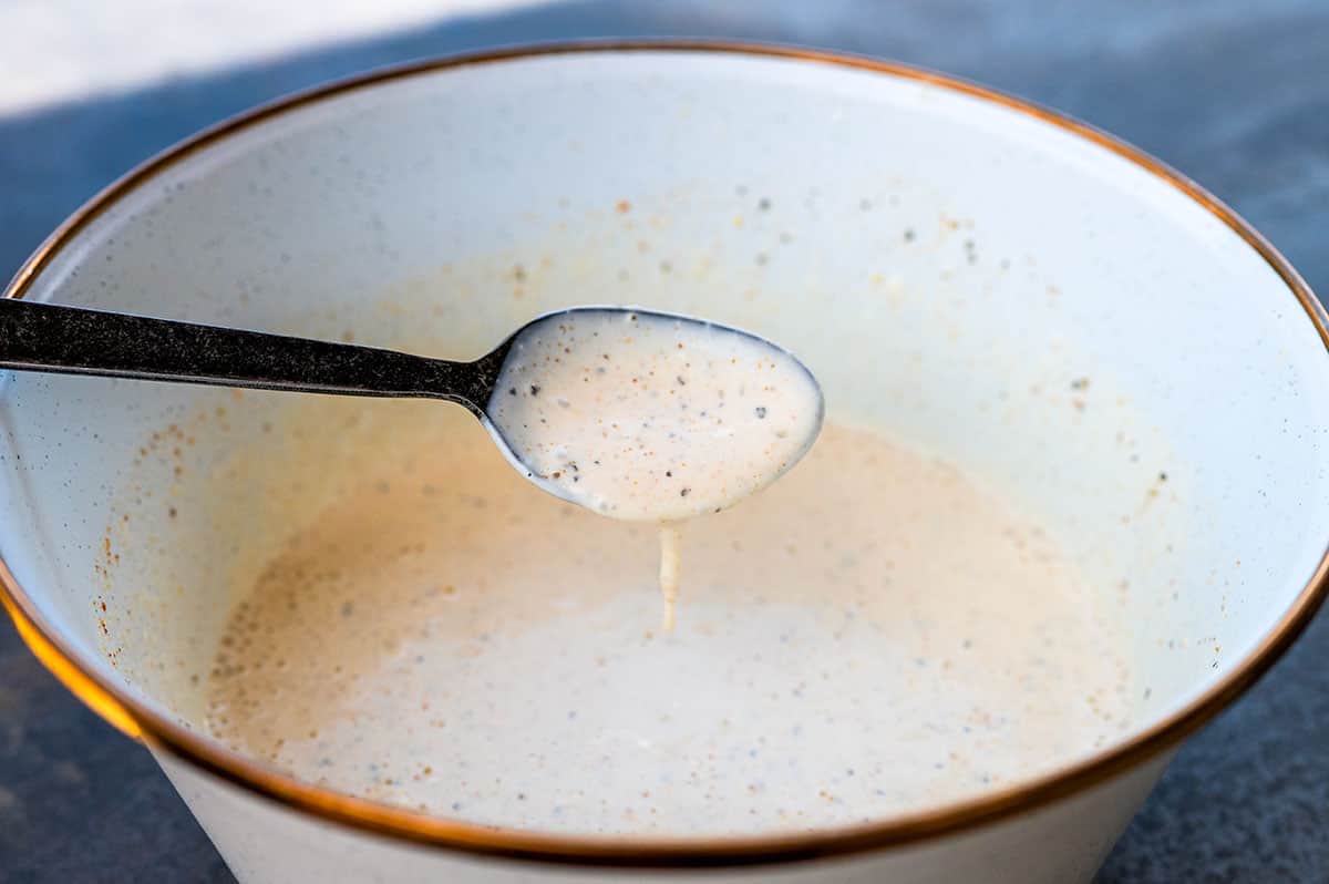 Spoon of Alabama White Sauce dripping into white bowl.