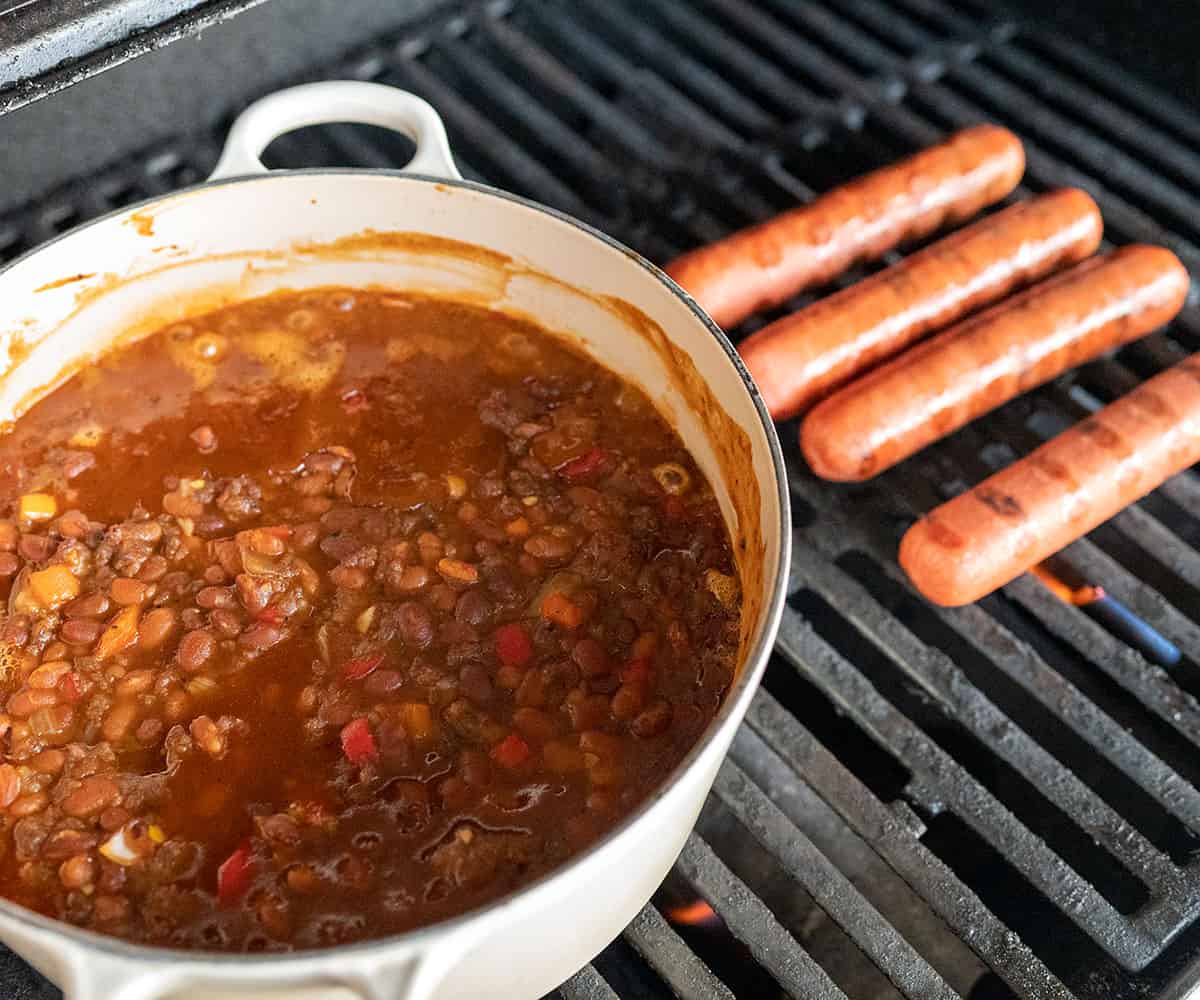 Baked beans in pot on grill with hot dogs.