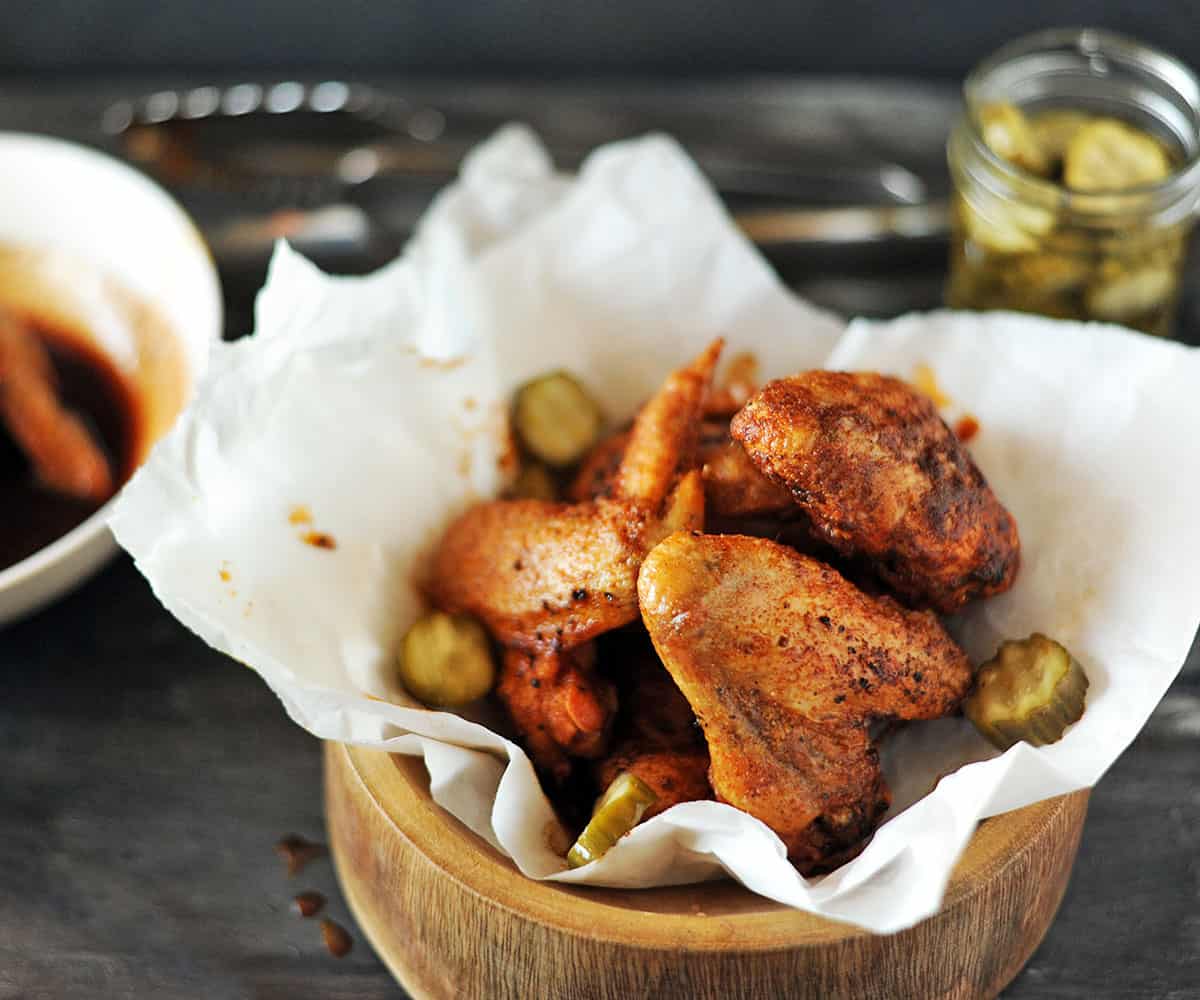 grilled Nashville hot chicken wings in bowl with pickles.