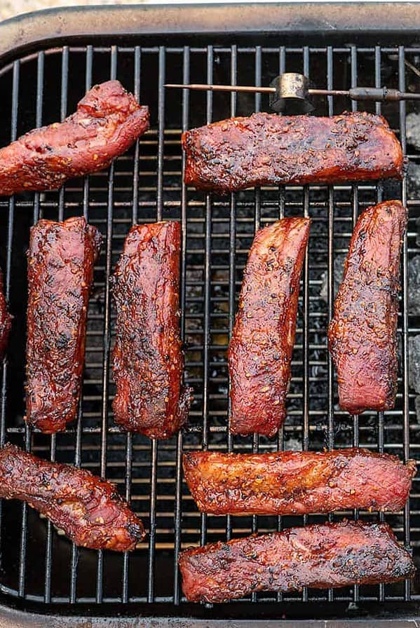 Individually Smoked Pork Ribs on a PK Grill with charcoal to the side.