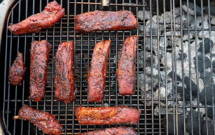 Individually Smoked Pork Ribs on a PK Grill with charcoal to the side.