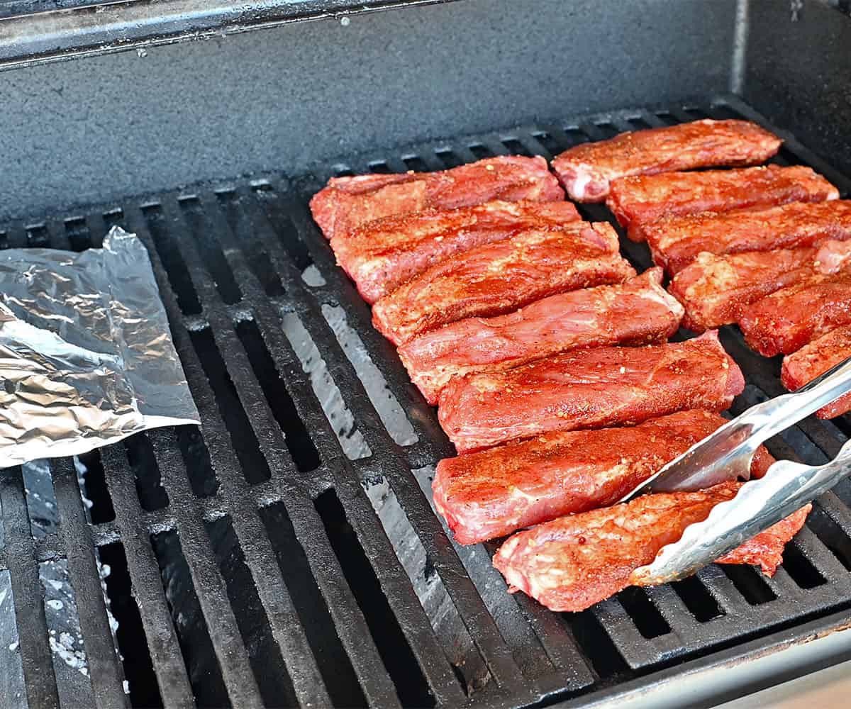 Individually Smoked Pork Ribs on a gas grill near a foil pouch.