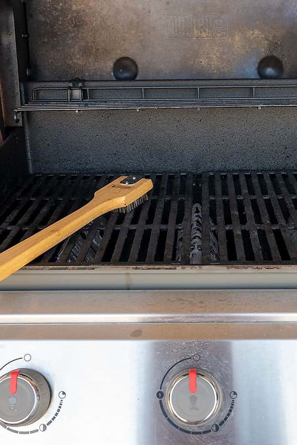 dirty gas grill with grill brush lying on grate.