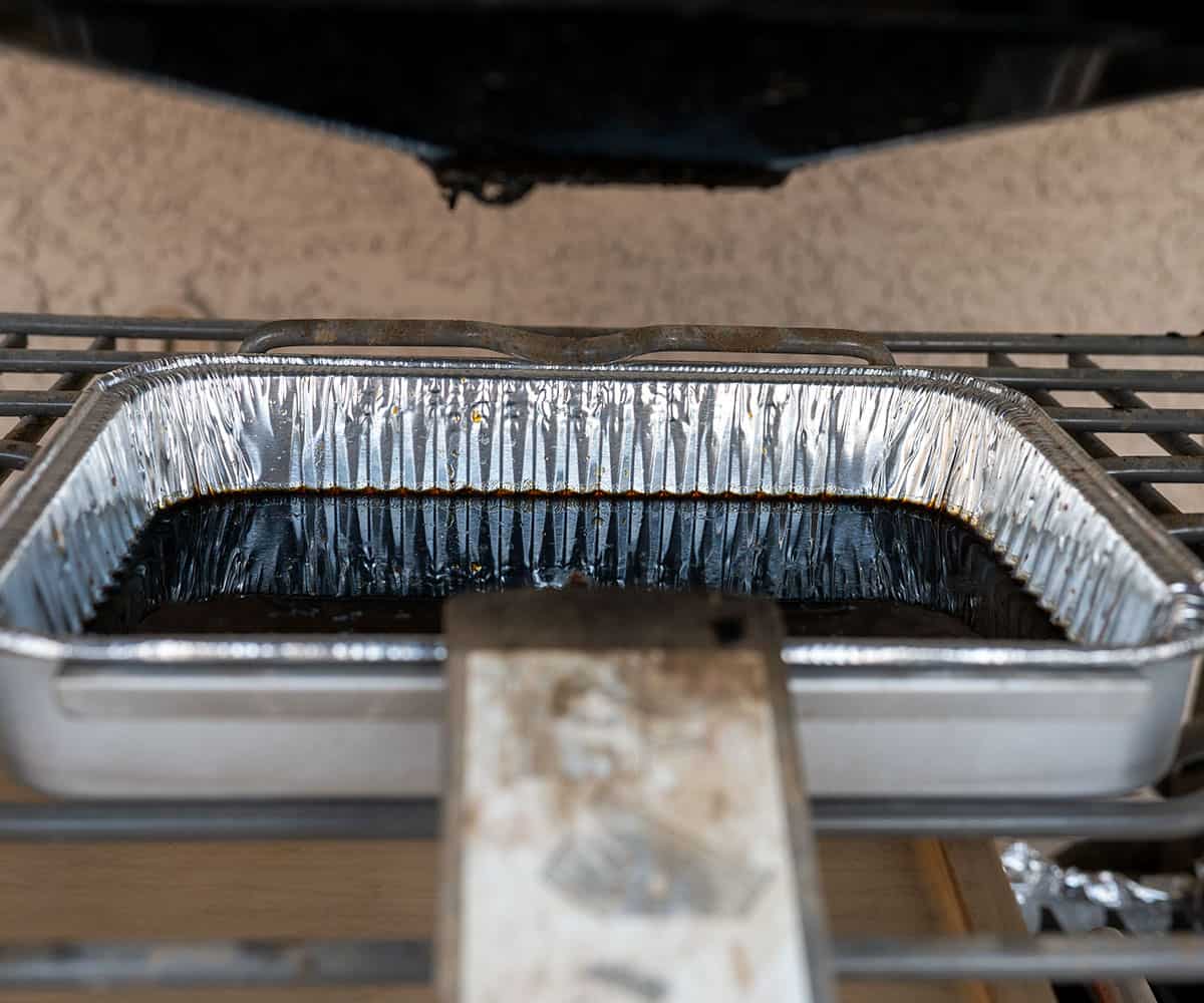 gas grill drip pan filled one quarter of the way with grease.
