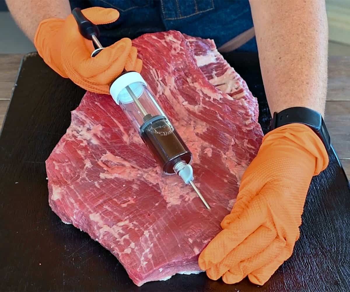 using a meat injector to inject beef broth into a brisket. 