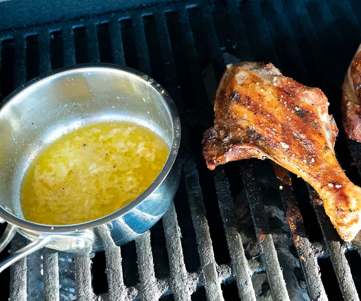 pot of lemon butter on grill next to turkey leg.