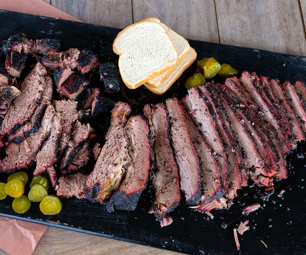 platter of sliced smoked beef brisket with pickles and white bread.