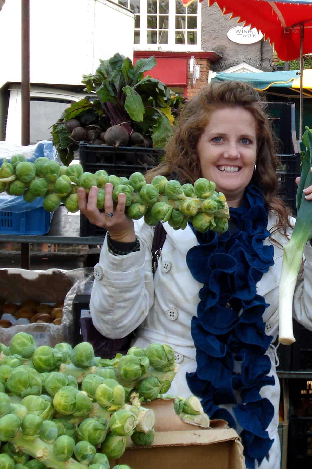 woman holding stalk of Brussels sprouts in market.