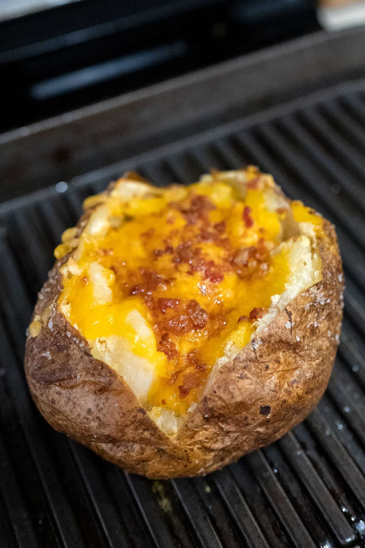 baked potato on Ninja foodi grill with melted cheese and bacon bits.
