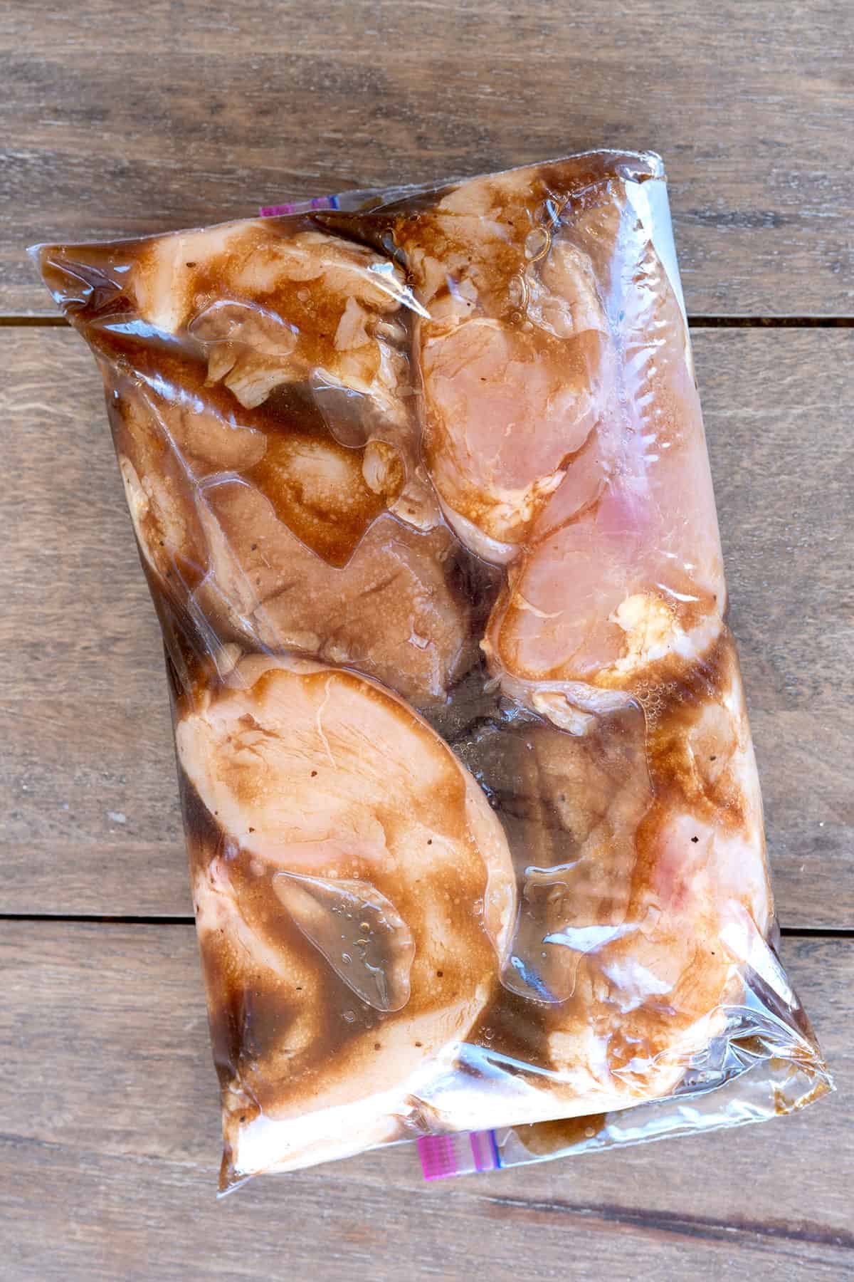 four chicken breasts marinating in plastic bag.