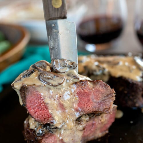 filet mignon steak cut in half being held by knife with mushroom sauce.