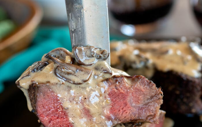 filet mignon steak cut in half being held by knife with mushroom sauce.