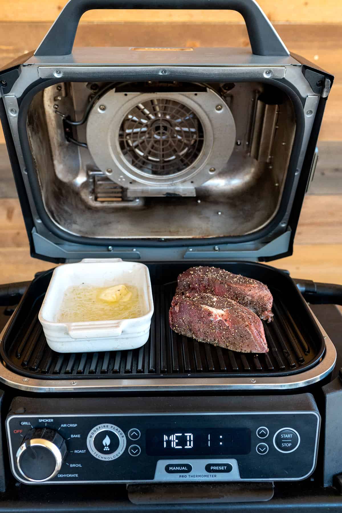 2 filet steaks on grill with small baking dish with melted butter on ninja grill.