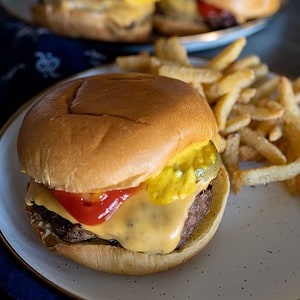 close up of grilled frozen hamburger on plate with fries.
