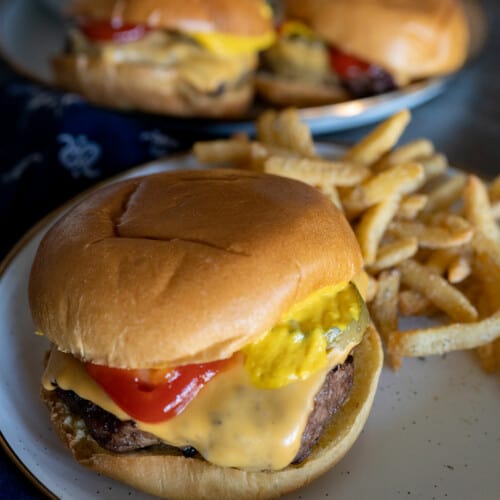 close up of grilled frozen hamburger on plate with fries.