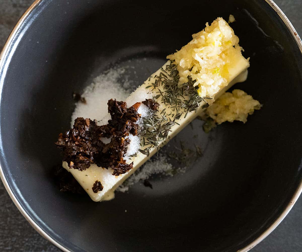 stick of butter in bowl with minced ancho, garlic, thyme and salt on top.