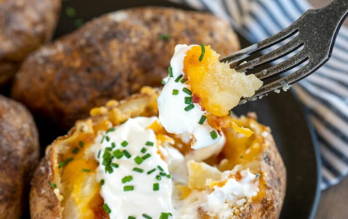 fork lifting bite of fully loaded baked potato.