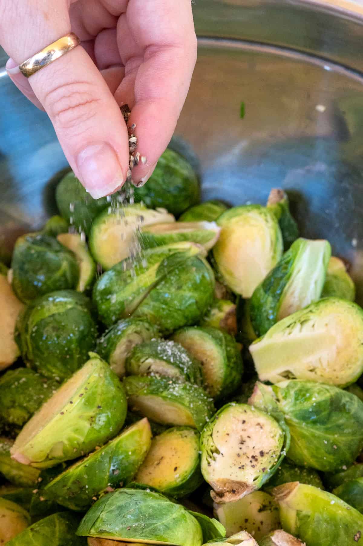 hand sprinkling black pepper on halved brussels sprouts.