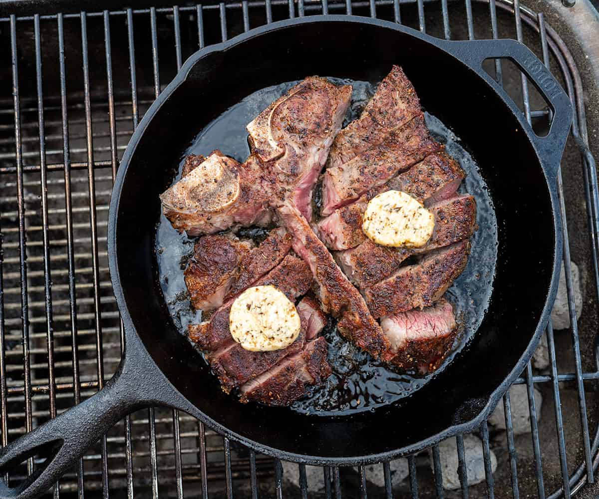 sliced porterhouse steak in cast iron skillet topped with compound butter.