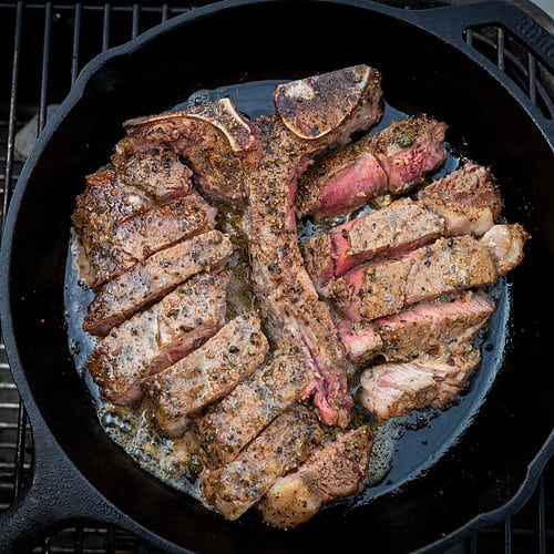 sliced porterhouse steak in skillet with melted compound butter.