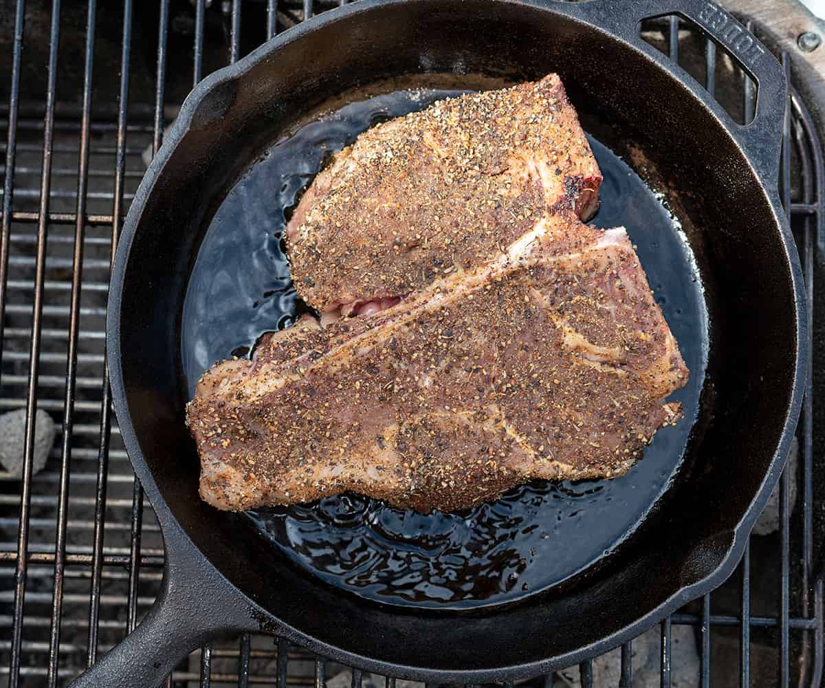 smoked porterhouse steak searing in cast iron skillet on grill.