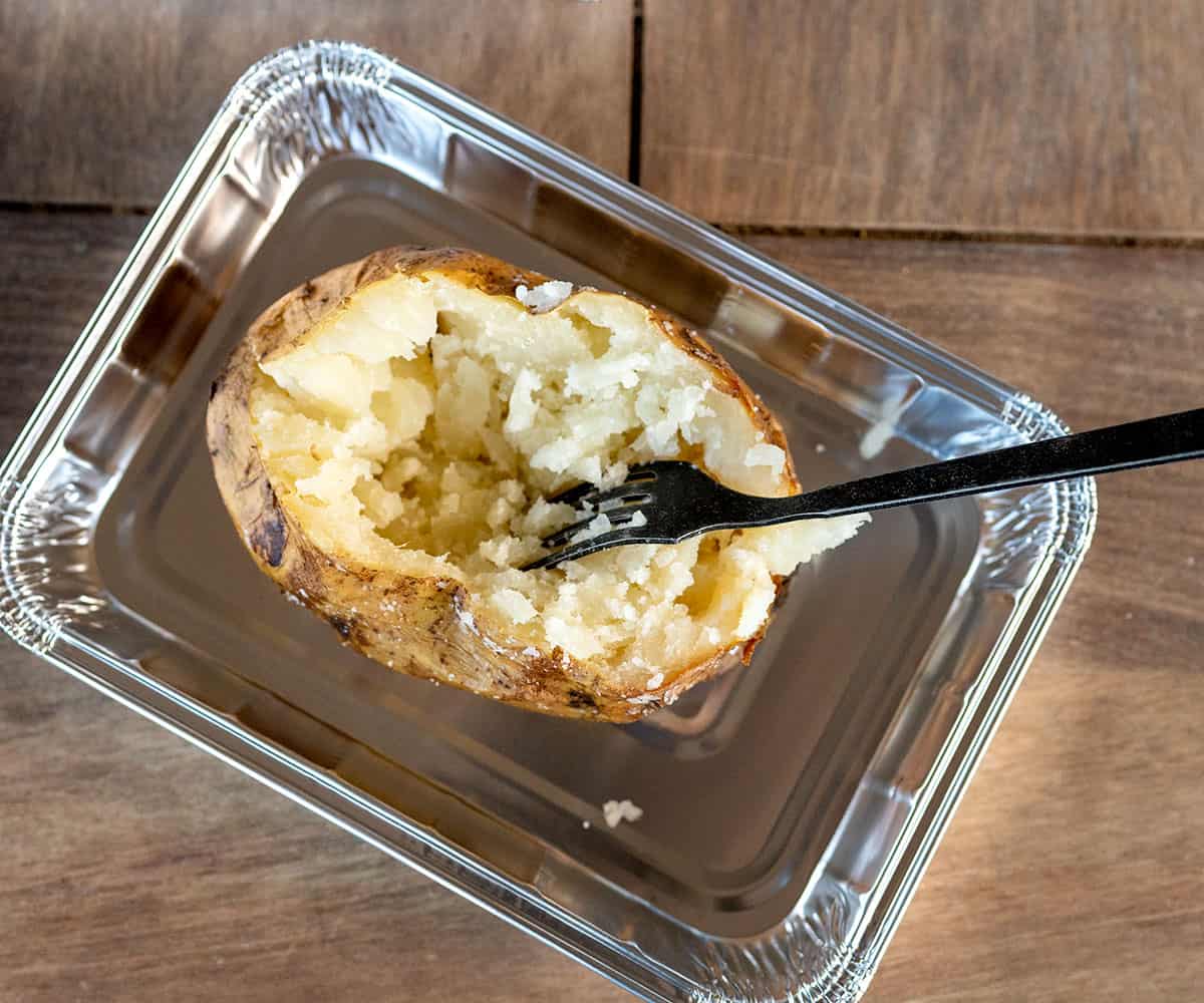 mashing inside of baked potato with fork.
