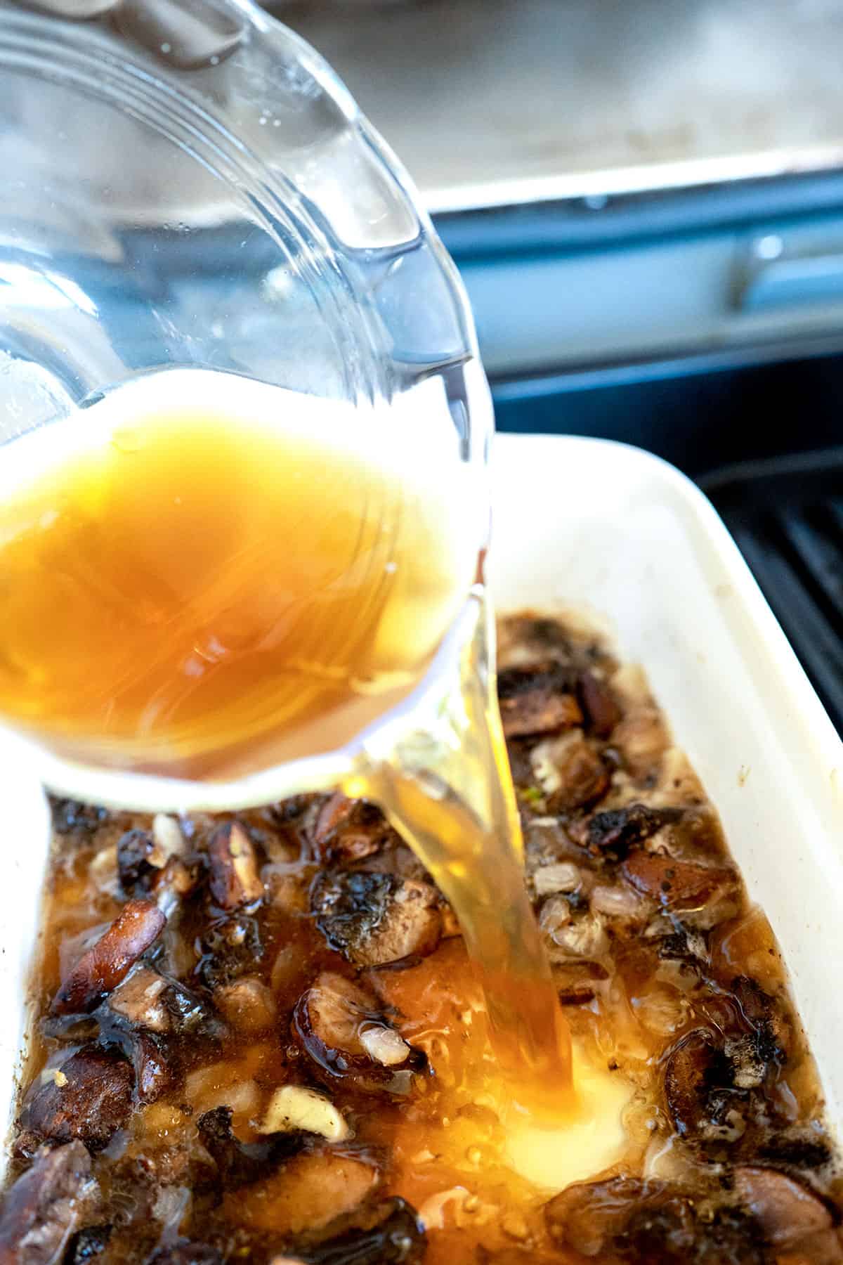 pouring beef broth into baking dish with mushrooms.