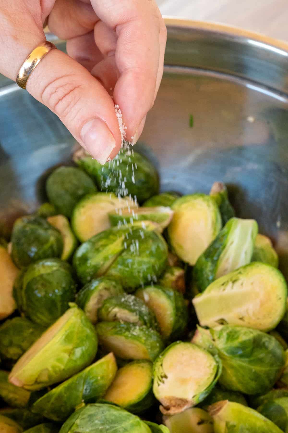 hand sprinkling kosher salt on halved brussels sprouts.