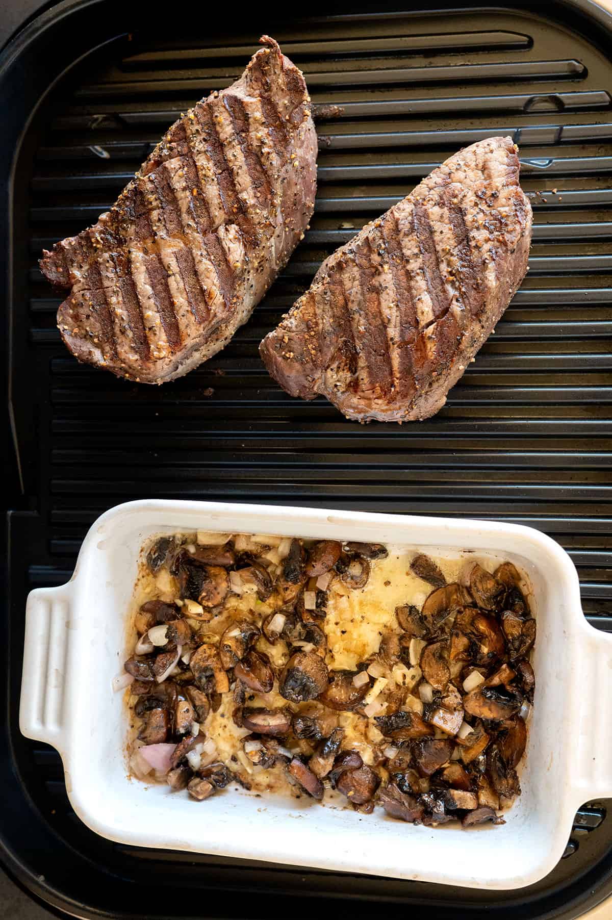 2 filet steaks on grill with small baking dish with sauteed mushrooms on ninja grill.